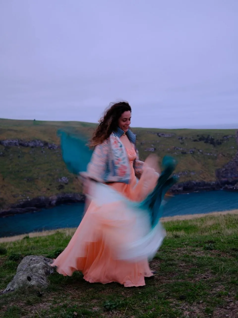 woman in peach dress on coastal mountain dancing with silk fans